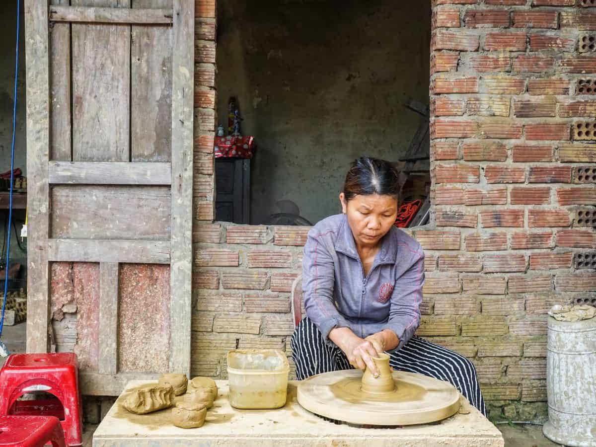 A female middle age worker is hand shaping pottery vase while sitting down at Ha Thanh pottery